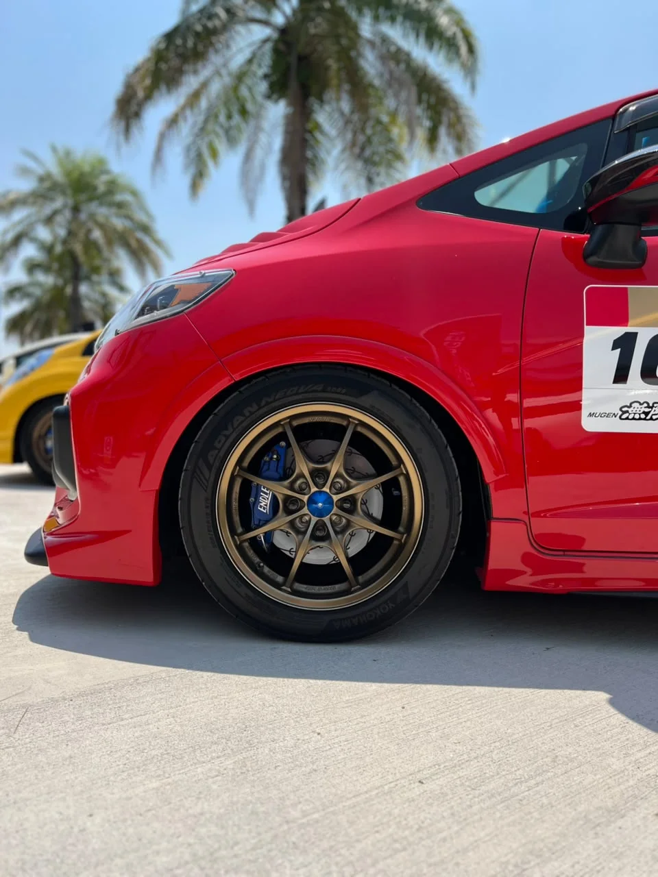 Red Honda with a bronze sport rim at an outdoor automotive event